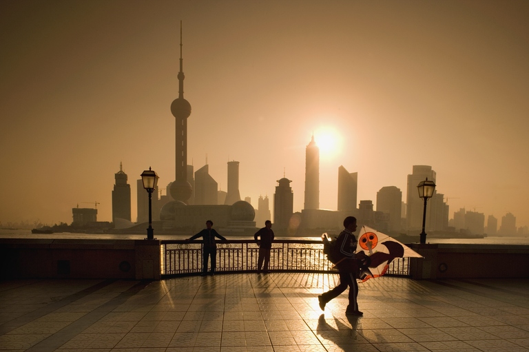 China. Shanghai. Skyline of Pudong (Business District). Background: Huangpo River.Foreground: People on Boulevard The Bund. Man in silhouette walking with kite.
